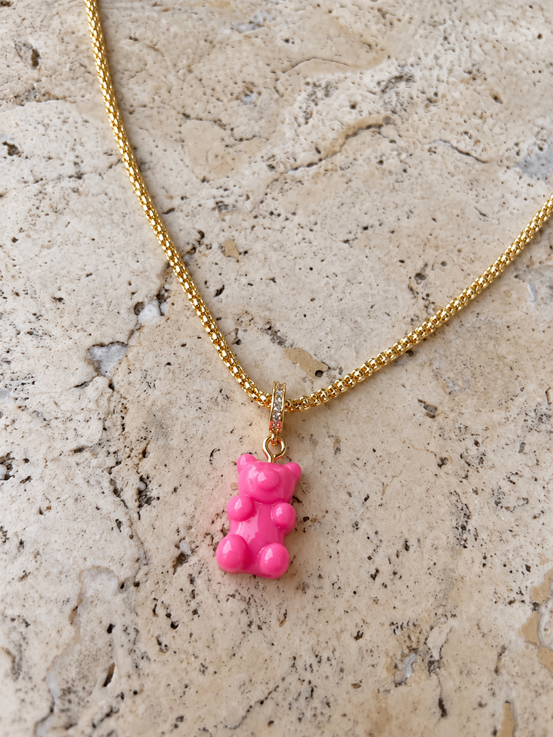 MONLANA Shiny Gummy Bear Necklace - Pink, featuring a gold chain and glossy pink gummy bear pendant on a natural stone background